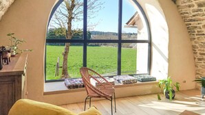 A cozy room with a large arched window, a wicker chair, a small table, and a view of a green field.