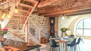 A dining area with a stone wall, wooden staircase, and a large arched window.