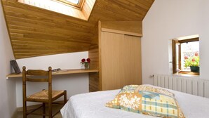 Une chambre avec un puits de lumière, un bureau en bois, une chaise, un lit avec un coussin à motifs et une fenêtre ornée de fleurs.