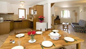 Un coin repas avec une table en bois dressée pour quatre personnes, une cuisine en arrière-plan et un salon avec un canapé et un téléviseur.
