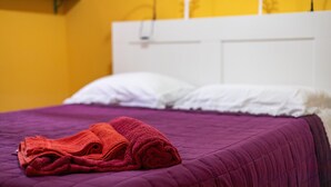 Un lit recouvert d’une couverture violette, avec une serviette rouge enroulée posée dessus.