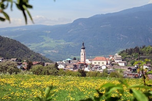 Une ville qui se distingue par son imposante tour, entourée de collines verdoyantes et d’un champ de fleurs jaunes.
