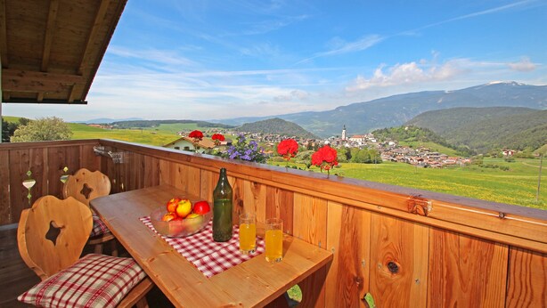 Un terrazzo in legno con tavolo, sedie e vista su una città e montagne.
