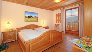 Camera da letto con struttura in legno, un letto, comodini, una finestra con tende, un quadro appeso al muro e una mensola di legno con giocattoli.