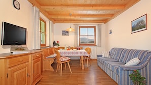 Un accogliente soggiorno con soffitto in legno, una televisione, un tavolo da pranzo con sedie, un divano e una pianta in vaso.
