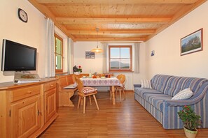 Un salon chaleureux avec un plafond en bois, un téléviseur, une table à manger avec des chaises, un canapé et une plante en pot.