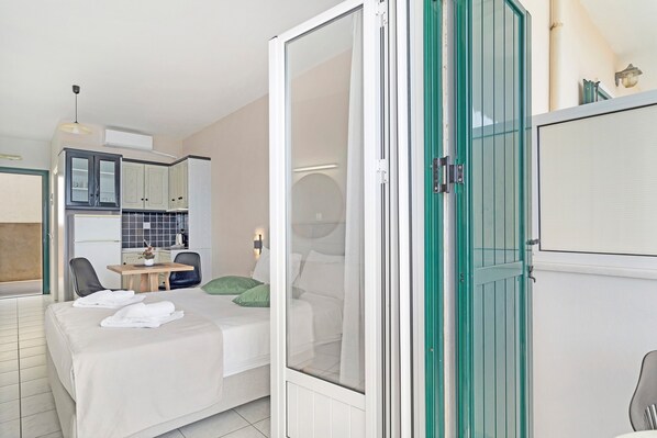 A modern hotel room with a bed, a desk, a chair, a kitchenette, and a sliding glass door. - Apartment in a Hotel 'Sunset Premium Studio A' with Sea View, Shared Pool, & Wi-Fi (Lefkada)