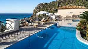 A pool with lounge chairs and umbrellas, a view of the sea, and a building with a tiled roof. - Apartment 'Sunset Premium Studio B' with Sea View, Shared Pool & Wi-Fi (Lefkada)