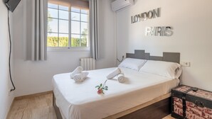 Una habitación de hotel con cama, ventana con cortinas, equipo de aire acondicionado, televisor montado en la pared y un objeto decorativo con la inscripción 'LONDON PARIS' en la pared.