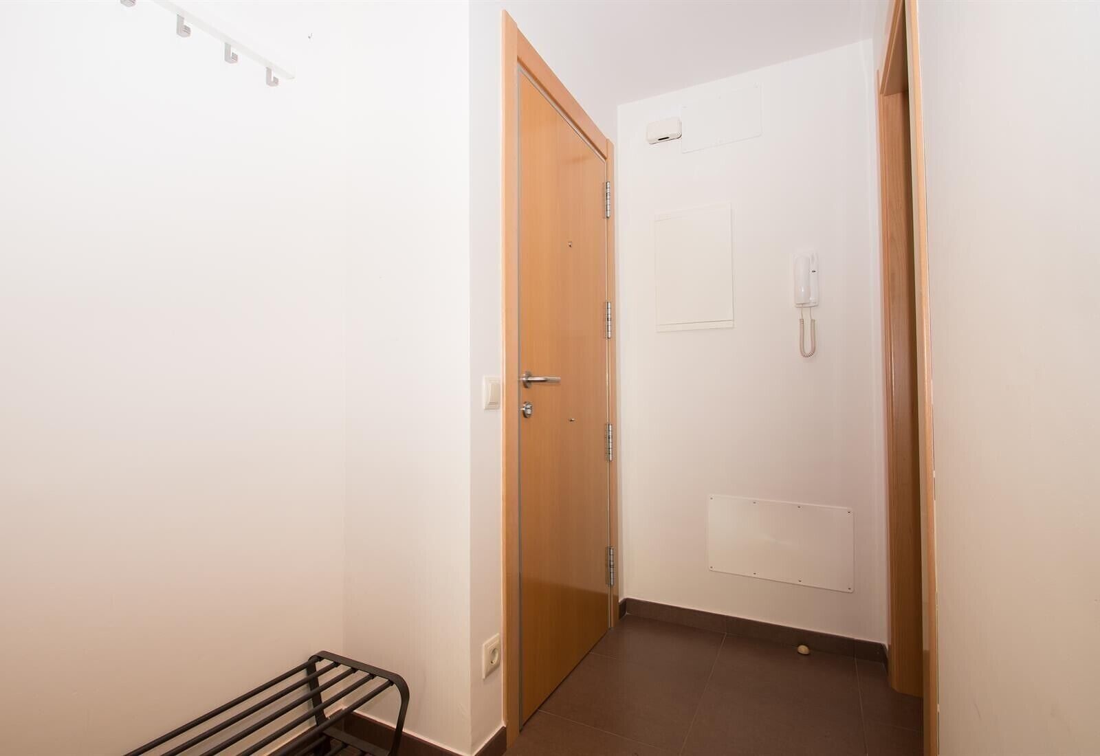 Un pasillo estrecho con una puerta de madera, una pared blanca y un pequeño estante negro.