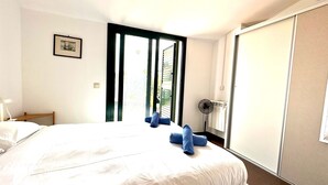 A hotel room with a large bed, a bedside table, a fan, and a view of the outdoors.