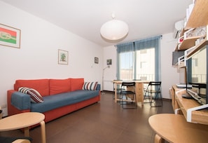 Un salon moderne avec un canapé rouge, une table à manger avec des chaises, un téléviseur et une grande fenêtre avec des rideaux.