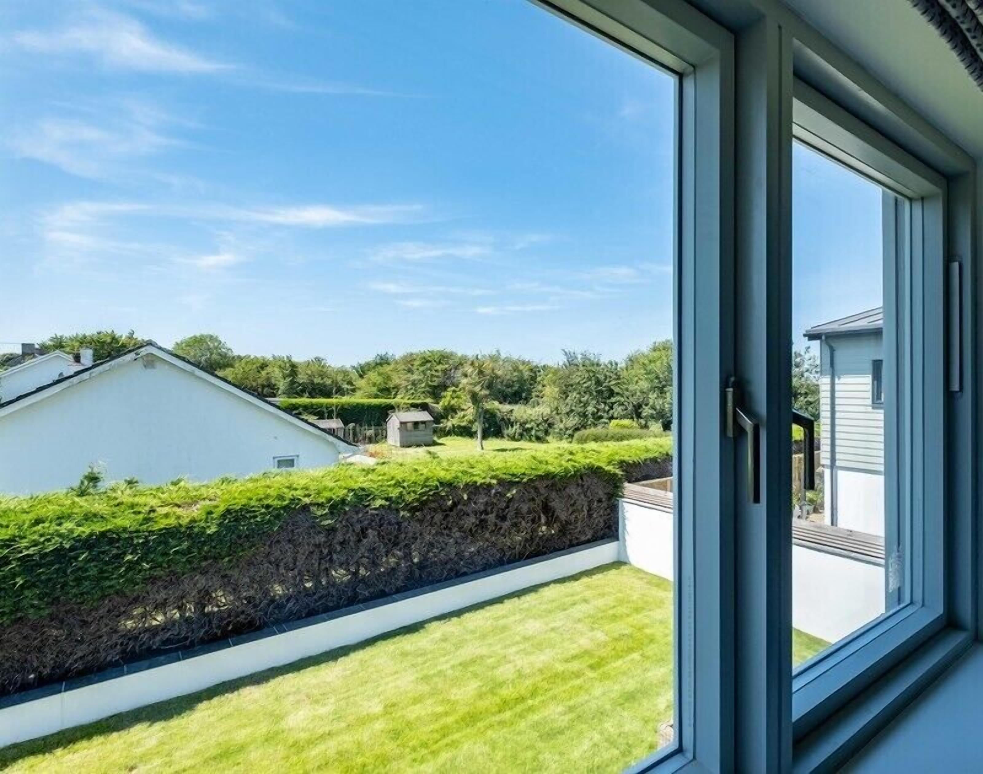 A view from a window overlooking a well-maintained lawn, a stone wall, and neighboring houses.