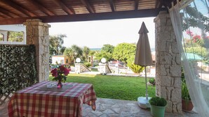 Un patio cubierto con una mesa a cuadros, pilares de piedra, una planta en maceta y vistas al paisaje.