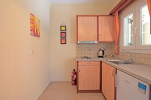 Une petite cuisine avec des meubles en bois, un évier et un réfrigérateur. Trois tableaux encadrés sont accrochés au mur.
