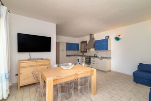 Un espace de vie compact comprenant un coin repas, une kitchenette et un téléviseur à écran plat fixé au mur.