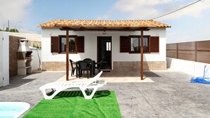 Une petite maison avec un toit en tuiles, une terrasse avec une piscine et du mobilier d’extérieur.