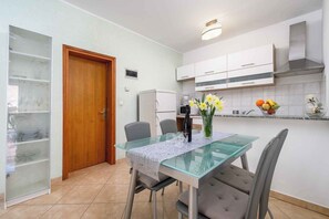 A modern kitchen with white cabinets, a glass dining table, and a wooden door. - Holiday apartment with internet, air conditioning, terrace and garden in a quiet location (Umag - Murine)