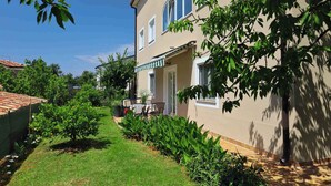 A two-story house with a garden, a patio with a table and chairs, and a covered entrance.