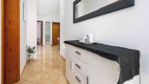 A hallway with a wooden door, a potted plant, a black countertop with a tray, and a mirror on the wall.