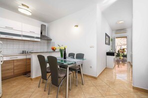 A modern kitchen with white cabinets, a stainless steel range hood, and a dining area with a glass table and chairs. - Holiday apartment with internet, air conditioning, terrace and garden in a quiet location (Umag - Murine)