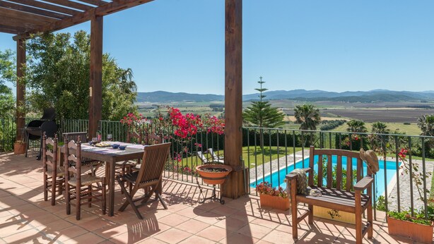 A covered patio with a table and chairs, a barbecue grill, a swimming pool, and a view of the countryside. - Villa Lino with Mountain Views, Pool, Garden, and Wi-Fi (Benalup Casas Viejas)