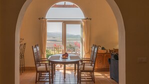 A dining area with a table and chairs, a view through a window, and a cabinet. - Villa Lino with Mountain Views, Pool, Garden, and Wi-Fi (Benalup Casas Viejas)