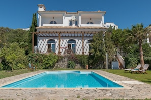 A large house with a swimming pool, a covered patio, and a staircase leading to the upper floors.
