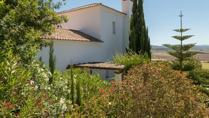 A white building with a tiled roof, surrounded by lush greenery and a clear view of the landscape. - Villa Lino with Mountain Views, Pool, Garden, and Wi-Fi (Benalup Casas Viejas)