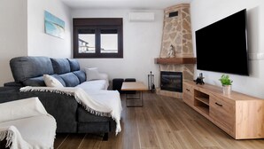 A modern living room with a sofa, a TV, a fireplace, and a stone accent wall. - Holiday Home 'Casa La Teja 2' with Pool and Wi-Fi (Vejer de la frontera)