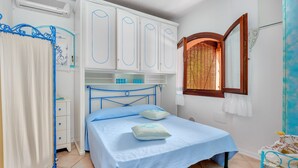 A bedroom with a bed, a wardrobe, a window, and a curtain. - Casa Turisarda Apartment with Shared Pool, Terrace, and Air Conditioning (Baja Sardinia)
