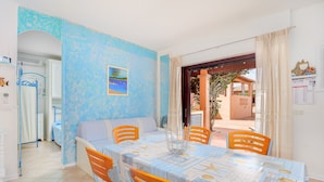 A dining area with a table set for four, a sofa, and a view of the outdoor area. - Casa Turisarda Apartment with Shared Pool, Terrace, and Air Conditioning (Baja Sardinia)