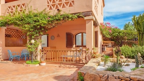 A building with a patio area, outdoor seating, and a cactus garden. - Casa Turisarda Apartment with Shared Pool, Terrace, and Air Conditioning (Baja Sardinia)