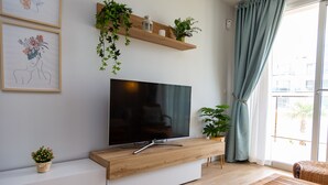 Un salon moderne doté d’un téléviseur à écran plat, d’une console en bois, de plantes en pot et offrant une vue sur l’extérieur grâce à une grande fenêtre.