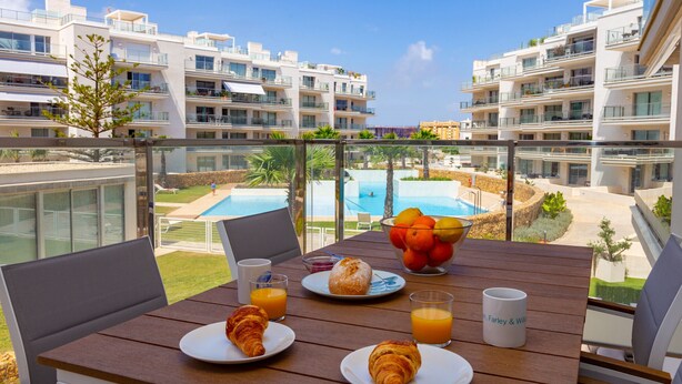 Un balcon avec des éléments pour le petit-déjeuner, une piscine et des bâtiments modernes en arrière-plan.