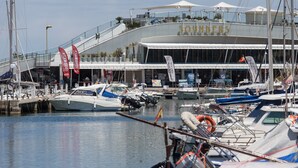 Un port de plaisance où sont amarrés de nombreux bateaux, un bâtiment portant l’inscription « SUNDERS », et plusieurs drapeaux.