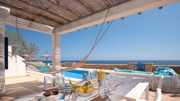 Un área de comedor al aire libre con vista al mar, una piscina y sillas de descanso.