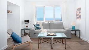 A modern living room with a grey sofa, a glass coffee table, a blue chair, and a view of the sea through large windows. - Holiday Home Villa Domus Alba B with Sea View, Pool, Garden & Wi-Fi (portocolom)