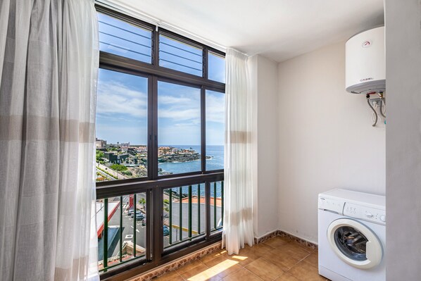 A balcony with a view of a coastal town, a washing machine, and a water heater.