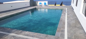 Une piscine rectangulaire à l’eau claire, entourée d’une terrasse carrelée et d’une rambarde.