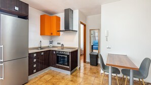 Cocina funcional con refrigerador, horno y armarios color naranja, que da paso a un comedor con mesa y sillas.