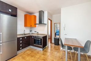 Une cuisine compacte équipée d’un réfrigérateur, d’un four et de meubles de couleur orange, qui donne sur un coin repas avec une table et des chaises.