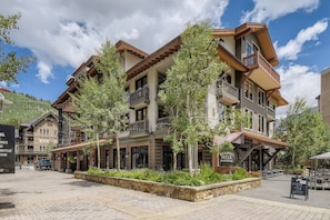 A multi-story building with balconies, a stone-paved plaza, and outdoor seating. - The Mill Club has it all!! Ski In/Ski Out, 3 King Beds, Queen Sofa Sleeper, Garage and Common Hot Tub. The Heart of Center Village!! (Copper Mountain)