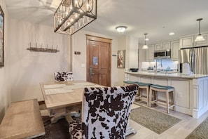 A modern kitchen with stainless steel appliances, a dining area with a wooden table and patterned chairs, and a pendant light fixture.