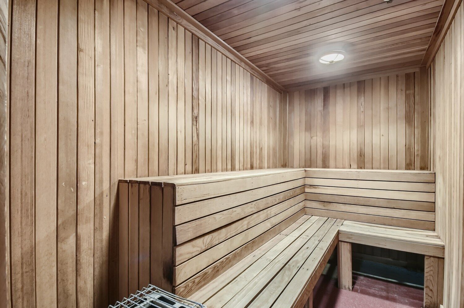 Una sauna con paredes y bancos de madera, una luz en el techo y un ventanal pequeño.