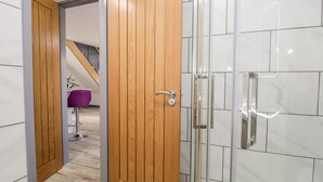 Ein modernes Badezimmer mit Holztür, Duschkabine aus Glas und weißen Fliesen.
