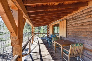 Eine Holzterrasse mit Tisch und Stühlen, umgeben von Holzwänden, mit Blick auf einen bewaldeten Bereich.