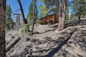 Eine rustikale Holzhütte mit einer Holzterrasse, umgeben von Kiefern und felsigem Gelände.