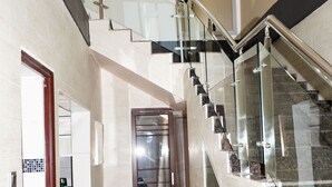 A modern interior with a glass railing staircase, a hallway leading to a door, and a wall-mounted light fixture. - Beautiful Two Bedroom Double Storey Apartment (Lusaka)