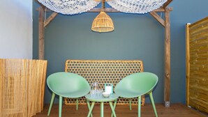 A room with a wooden floor, a woven wall, and a table with two green chairs. - Bungalow (Saint Paul)